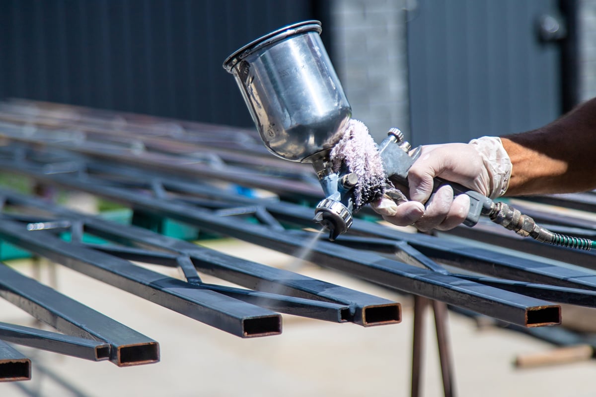 Technician spray coating a metal component with a powder gun
