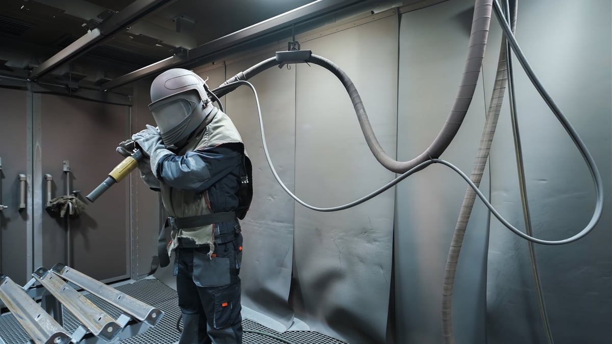 Operator sandblasting a steel workpiece with abrasive media